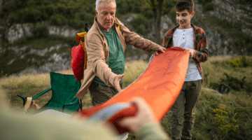 Father teaching his son how to care for a sleeping bag after using it during a camping trip