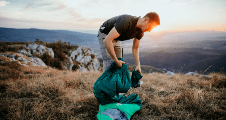man repairing his sleeping bag during a backpacking trip