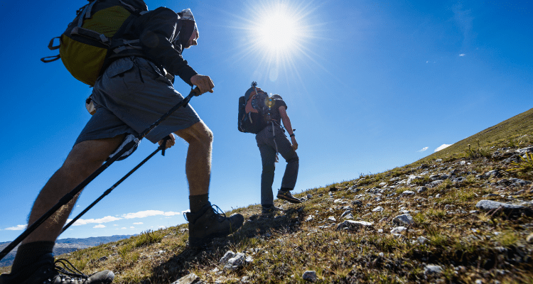 Pair of hikers with one utilizing two trekking poles while ascending a mountain