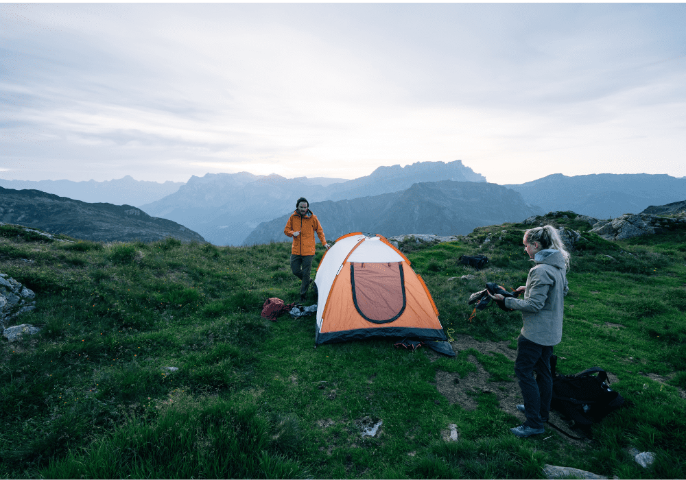 Husband and wife setting up camp on top of a mountain near sundown