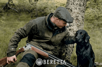 Man holding a beretta shotgun with his black lab dog